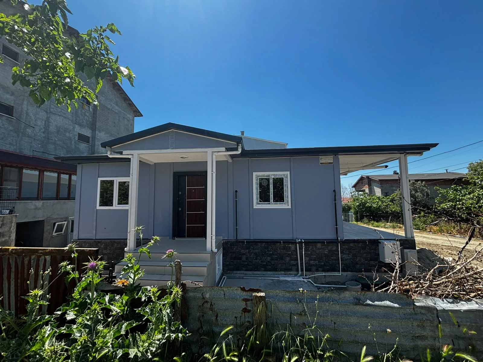 Gri cepheli, giriş sundurması ve yan verandası bulunan prefabrik ev
